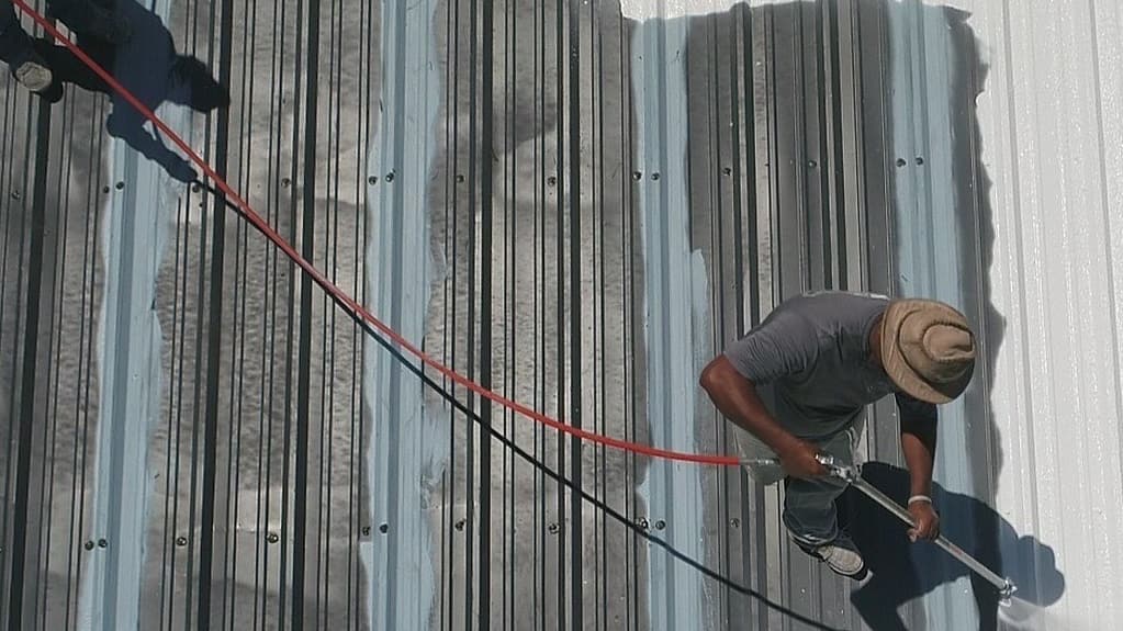 A Person painting a metal roof with a sprayer