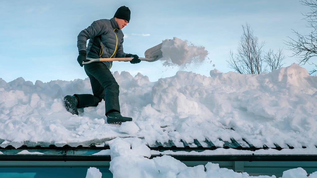 Person cleaning snow buildup on a low pitch roof