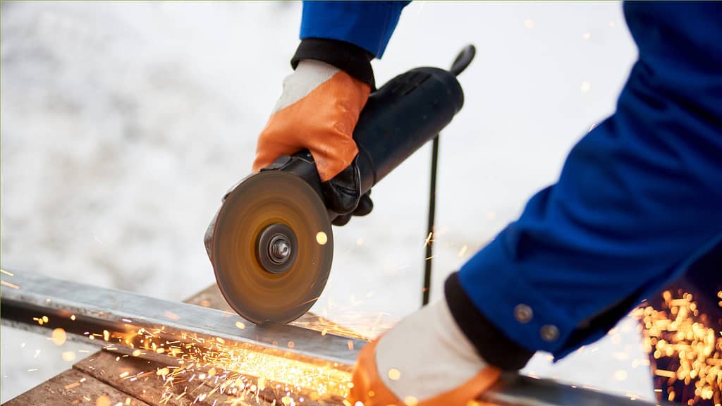 Worker using angle grinder to cut metal