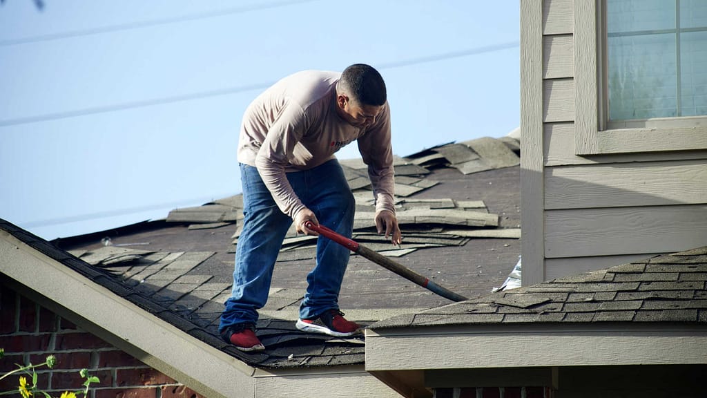 Person removing old asphalt shingles from a roof