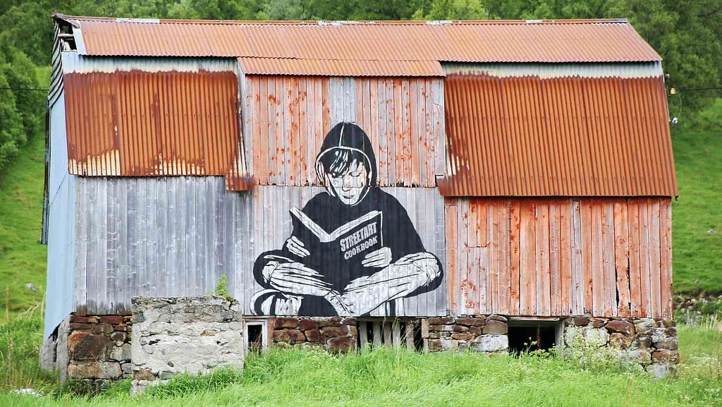 Person reading book on side of metal building with metal roof