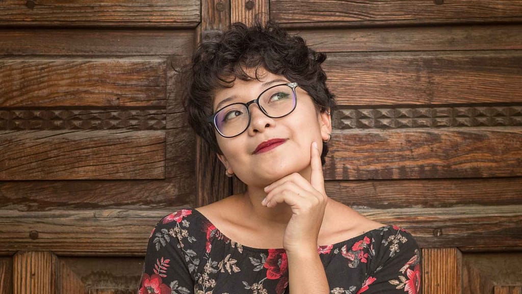 Person with glasses and dark hair thinking with wood background