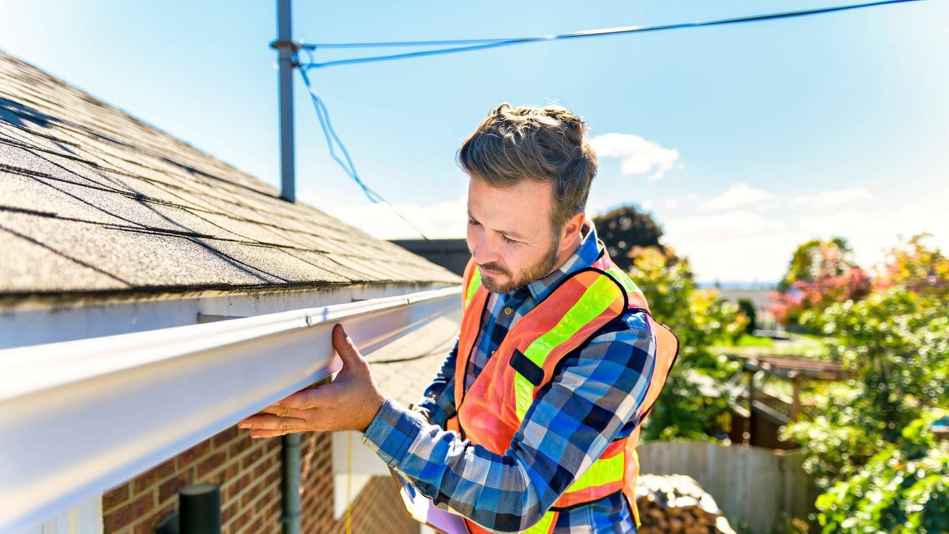 roofer in orange safety vest inspecting gutter