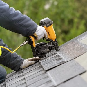 A Roofing contractor with a nail gun setting an asphalt shingle