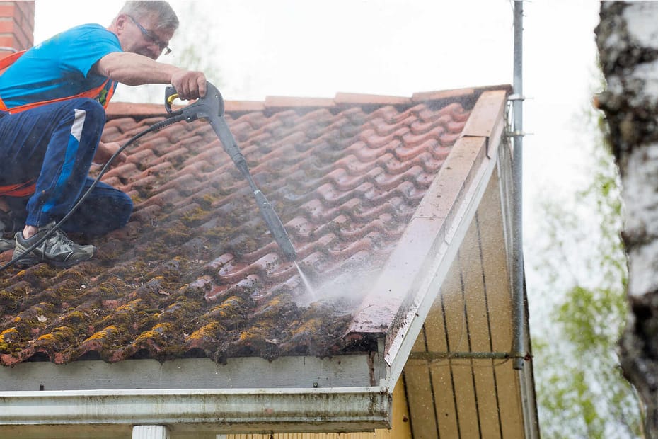 Roofer rinsing roof tiles covered in moss