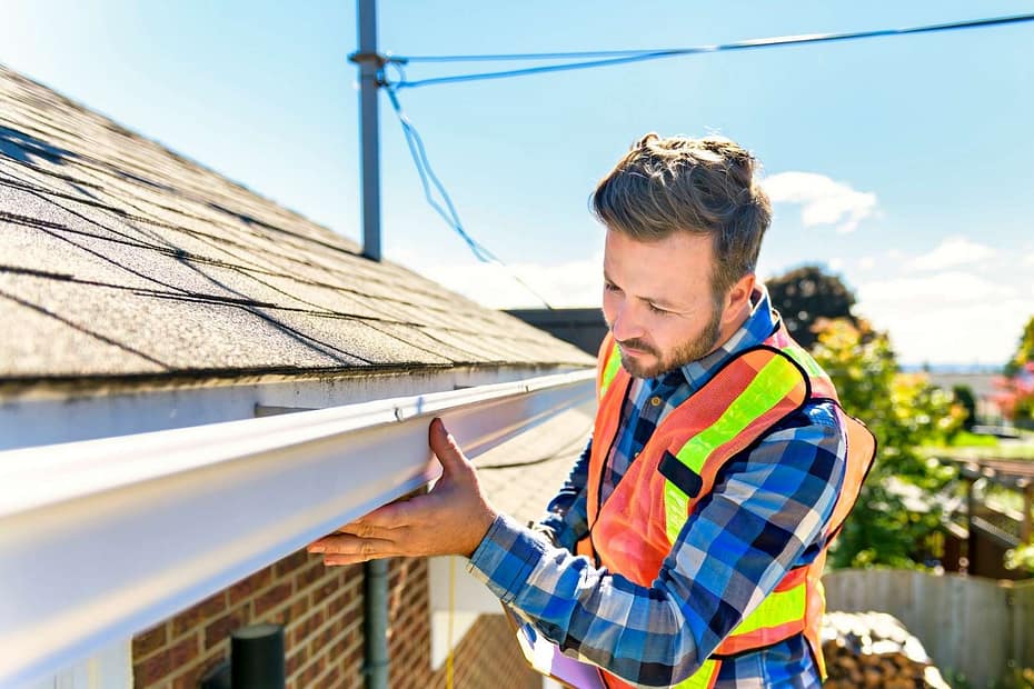 roofer in orange safety vest inspecting gutter