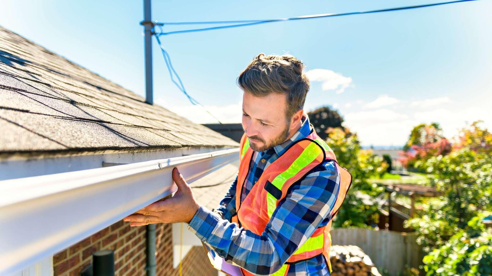 roofer in orange safety vest inspecting gutter