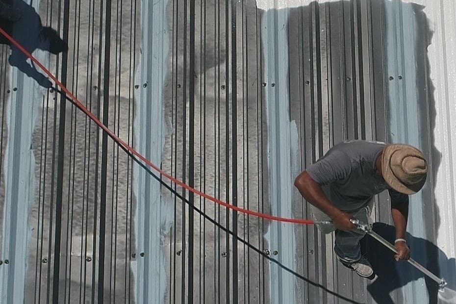 A Person painting a metal roof with a sprayer