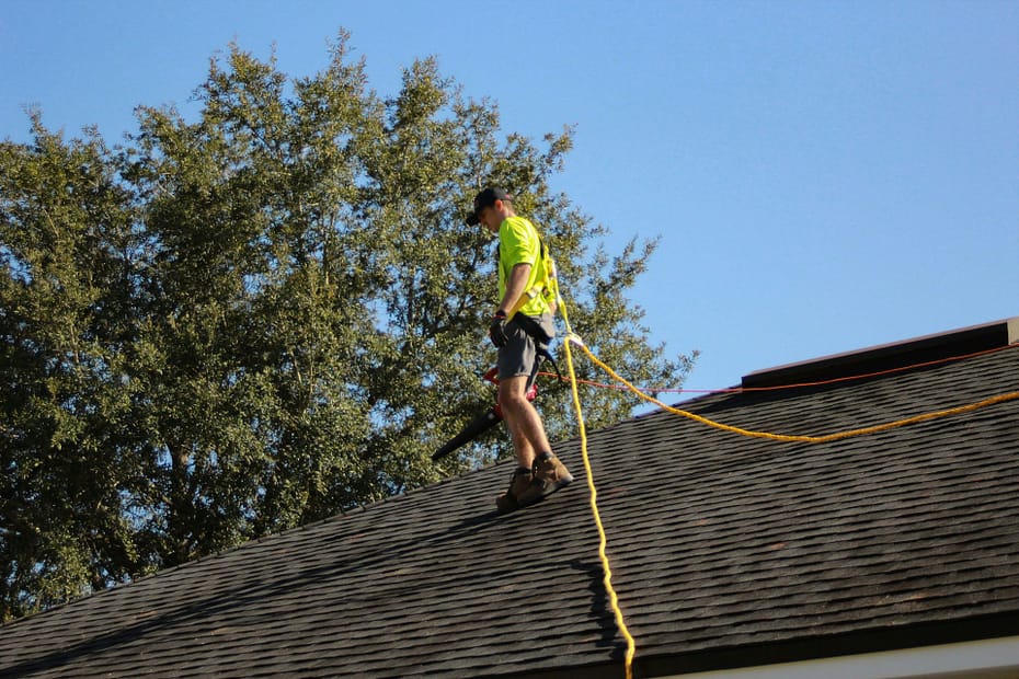 roofer walking on residential roof with safety harness.