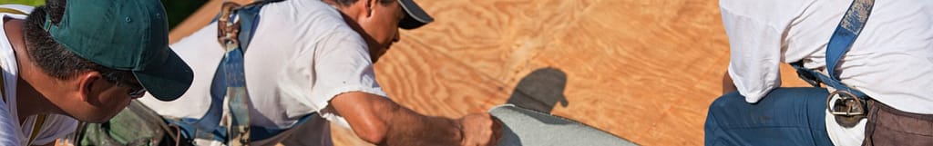 three harnessed roof workers laying material