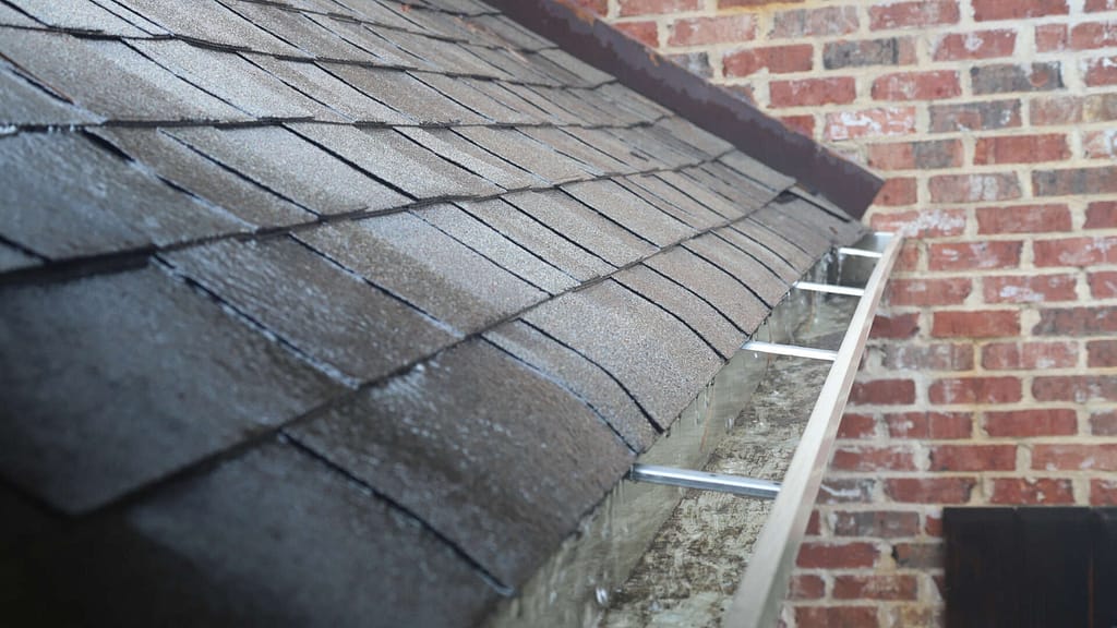 Gutter With Water Flowing From Asphalt Shingles During Rain Storm