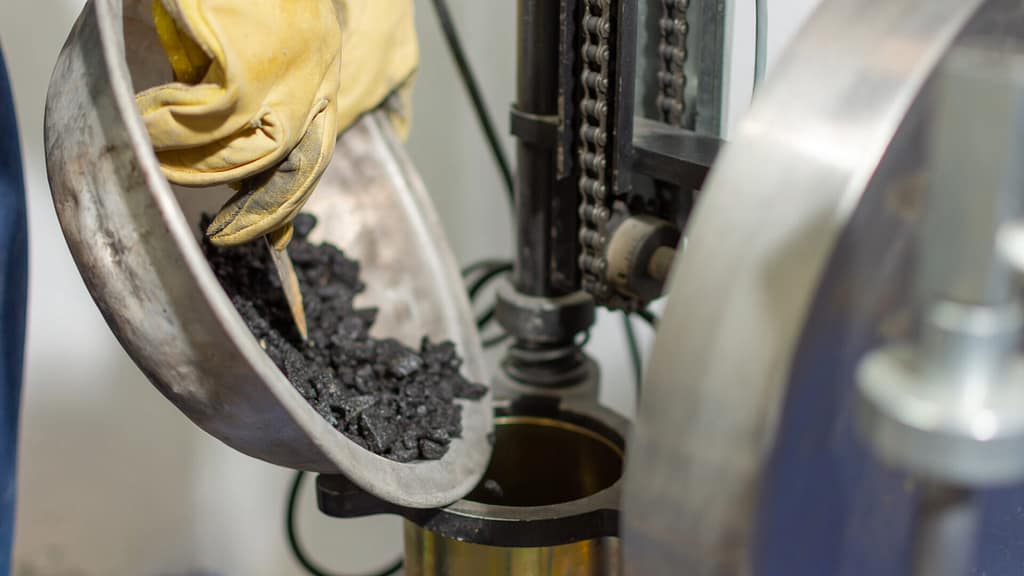 Person with protective gloves pouring asphalt into a machine