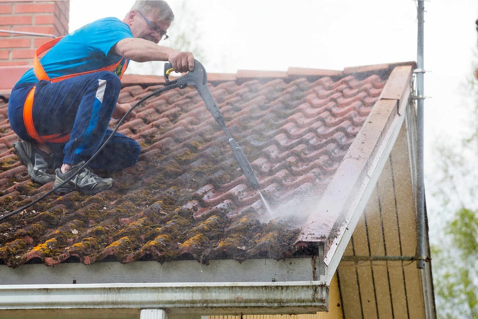 Roofer rinsing roof tiles covered in moss